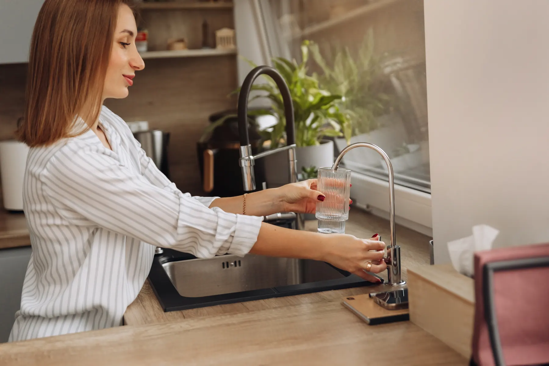 Person filling a glass at a slim faucet beside a kitchen sink