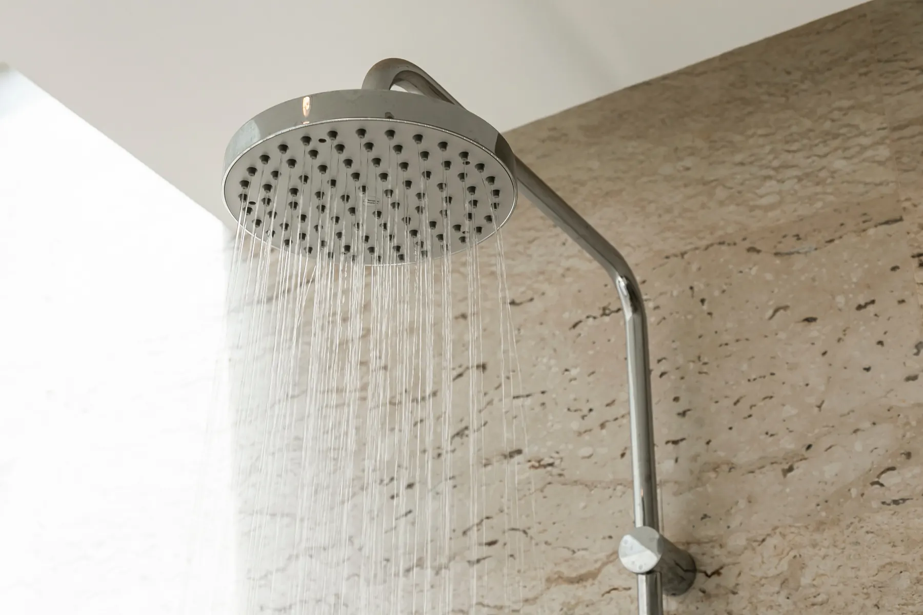 Rain shower head spraying water against a pale stone wall