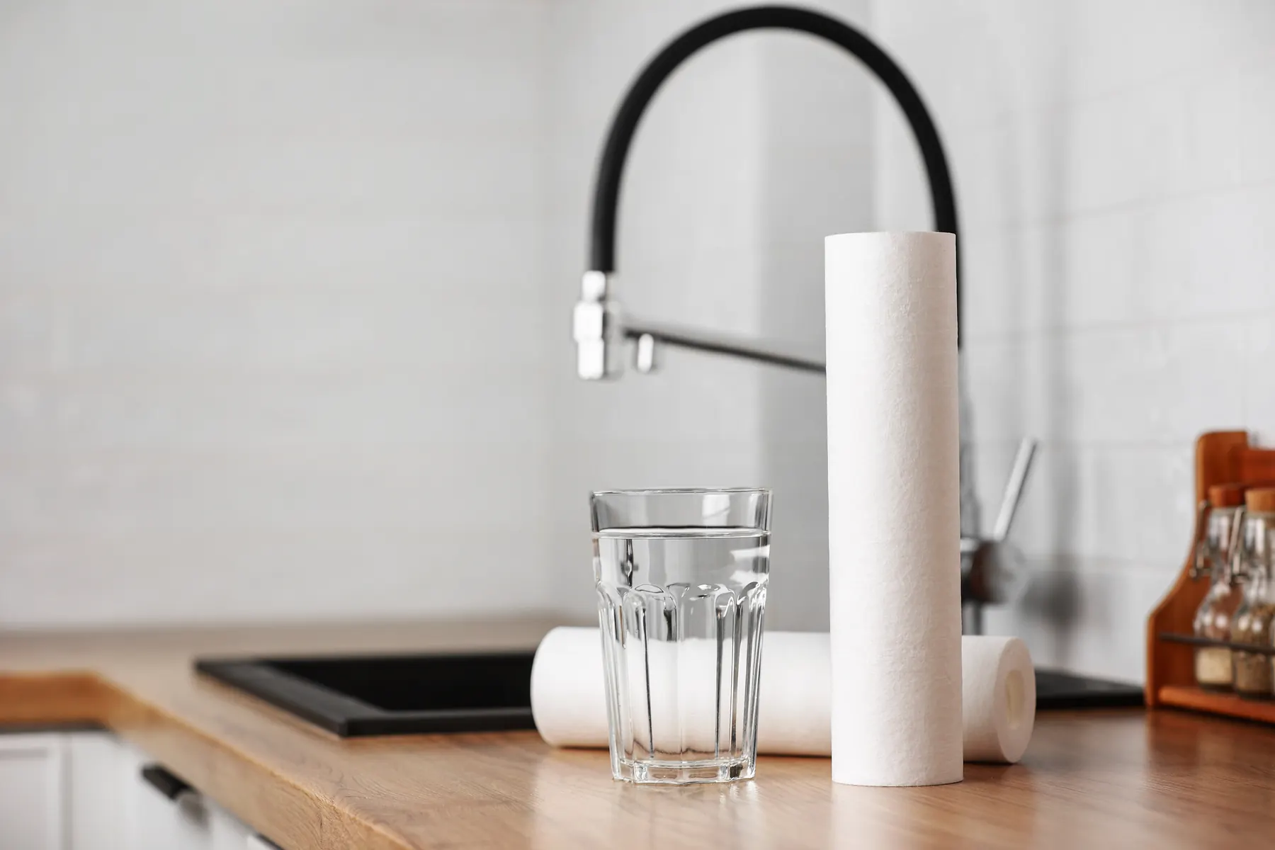 Black gooseneck kitchen faucet with a filled glass beside it