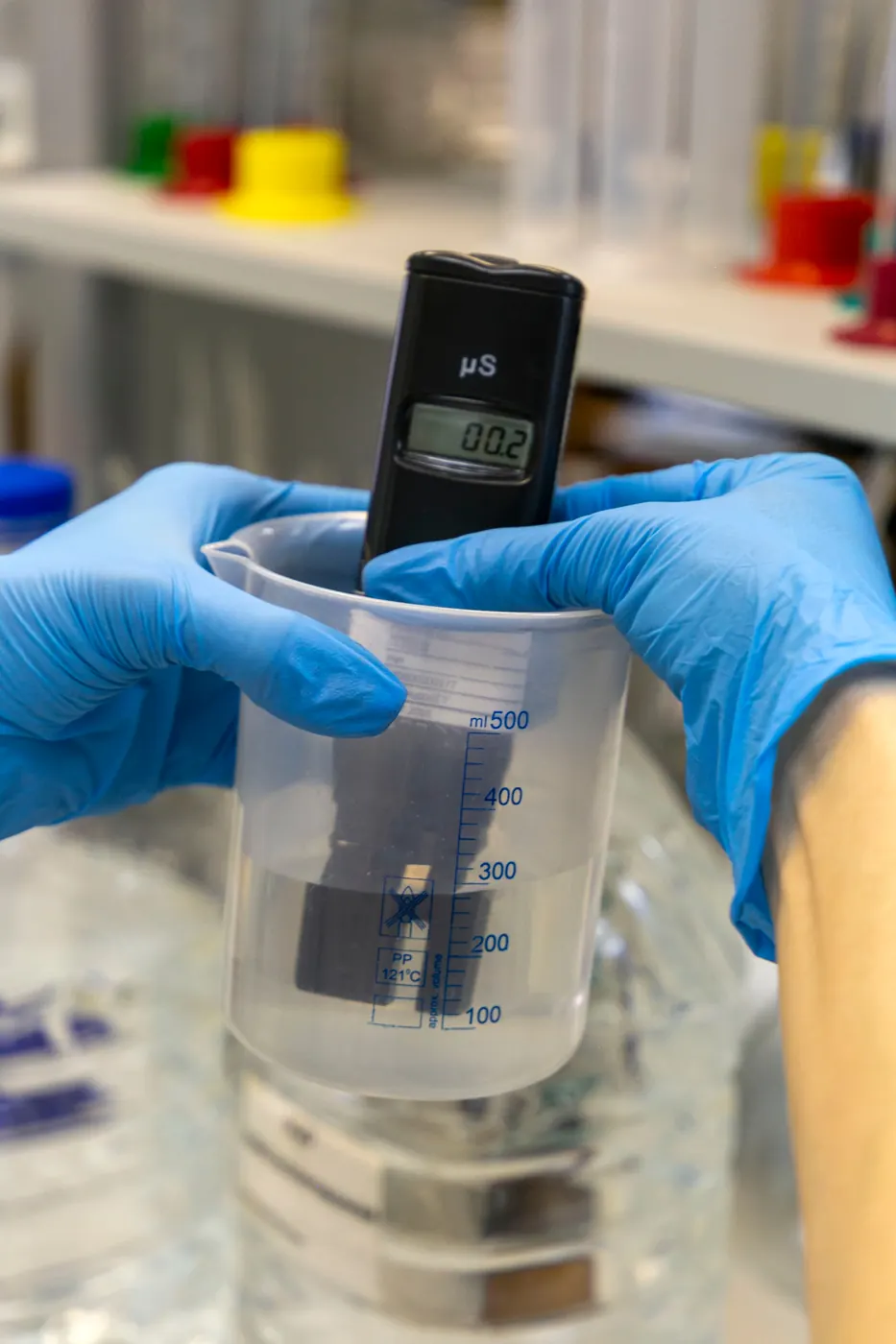 Gloved hands holding a digital water meter in a beaker of water