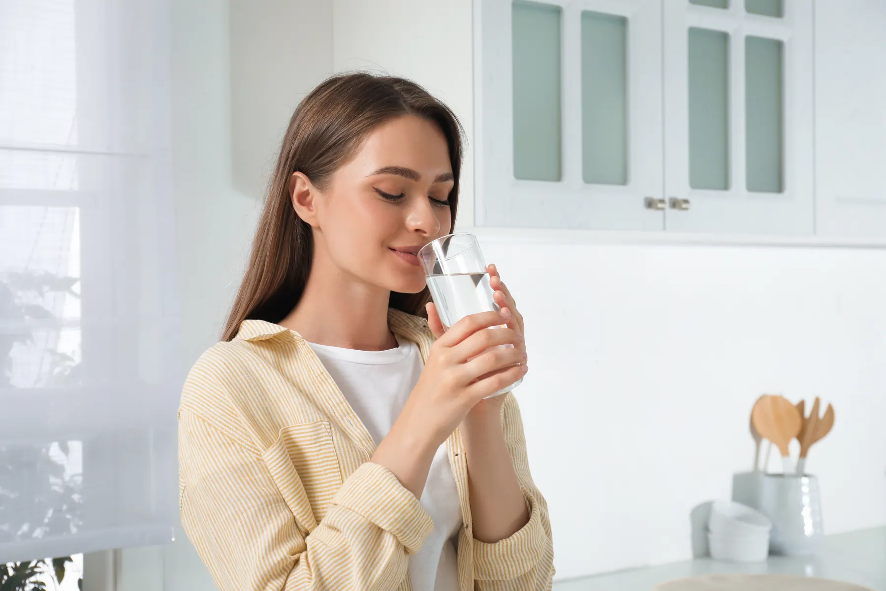 Person sipping water from a glass, in a bright white kitchen
